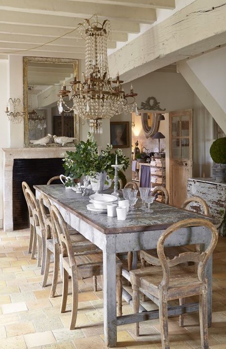 a shabby chic meets French farmhouse dining room with a statement crystal chandelier, shabby wooden furniture and greenery