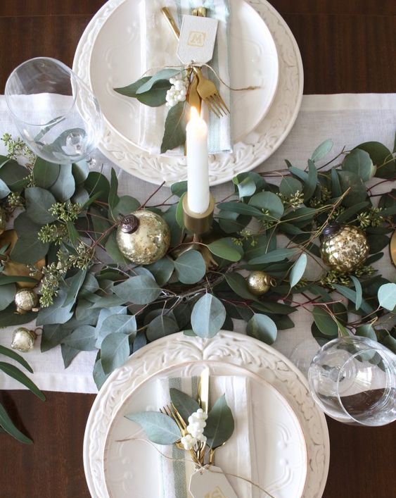 a simple and cute winter table with a greenery and gold ornament runner, white patterned porcelain and greenery and white berries on plates