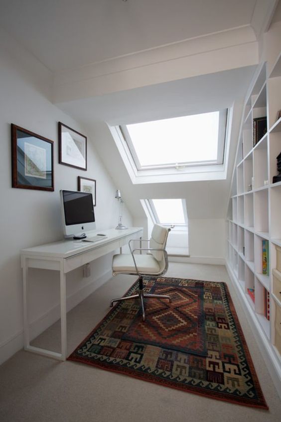 a small and sleek white attic home office with a narrow white desk and leather chair, a large storage unit, two skylights and a gallery wall