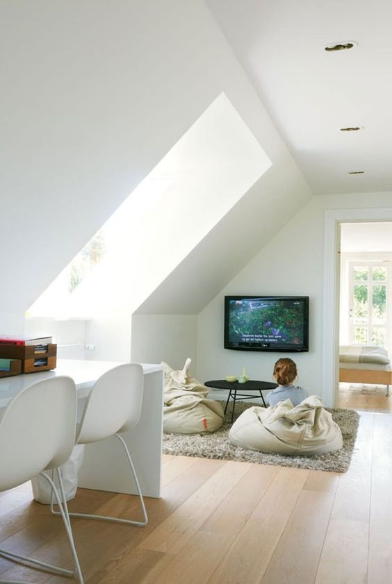 a small attic home office with a TV nook, a white shared desk and white chairs, a TV and beanbag chairs plus a large skylight