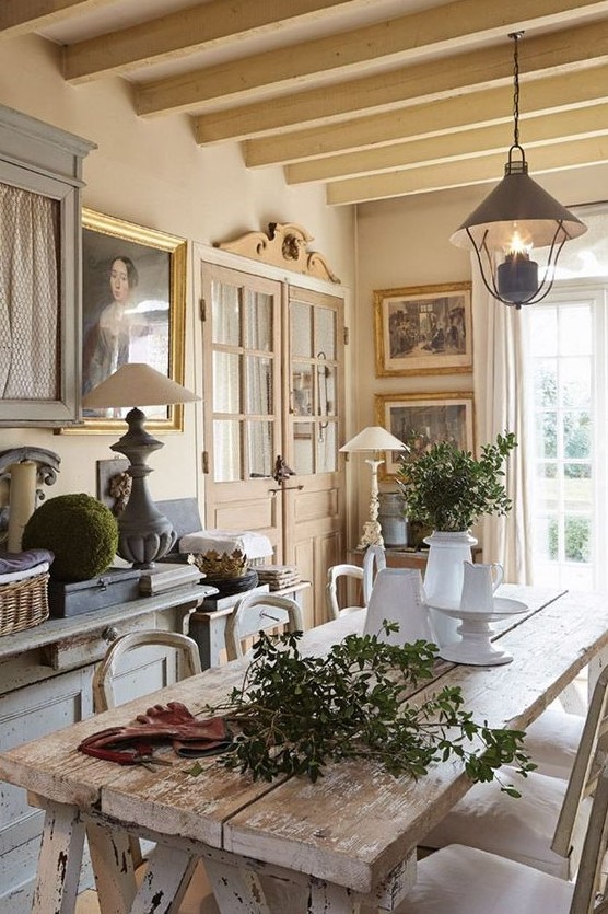 a sophisticated vintage French dining room with tan walls and a ceiling, a vintage storage unit, a shabby chic table and neutral chairs plus some art