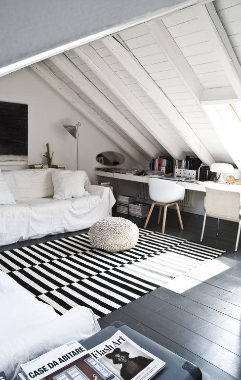 a stylish Nordic attic home office with a planked ceiling and floor, layered rugs, a couple of white sofas and a long shared desk plus a couple of chairs