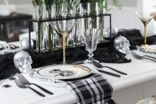 a stylish blackm white and silver Halloween tablescape with a black runner, plaid napkins, silver skulls, spiders and bold blooms