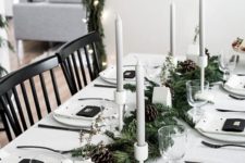 a stylish monochromatic winter table with an evergreen and pinecone runner, grey candles, white house vases, polka dot napkins