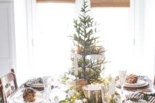 a stylish winter table with a Christmas tree, an evergreen and light runner and striped napkins