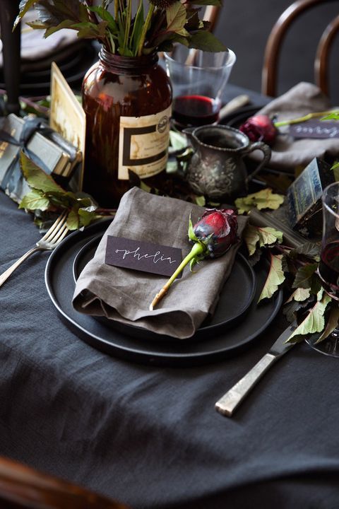 a vintage Halloween tablescape with black linens and plates, leaves and red roses, vases and candles
