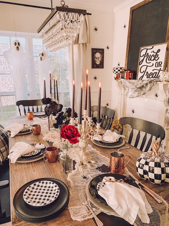 a whimsy Halloween tablescape with black and white plates, copper mugs, red and deep purple blooms, black candles