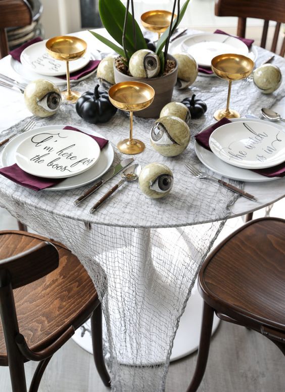 a wicked Halloween tablescape with cheesecloth, black pumpkins, white plates, purple napkins and large eyeballs