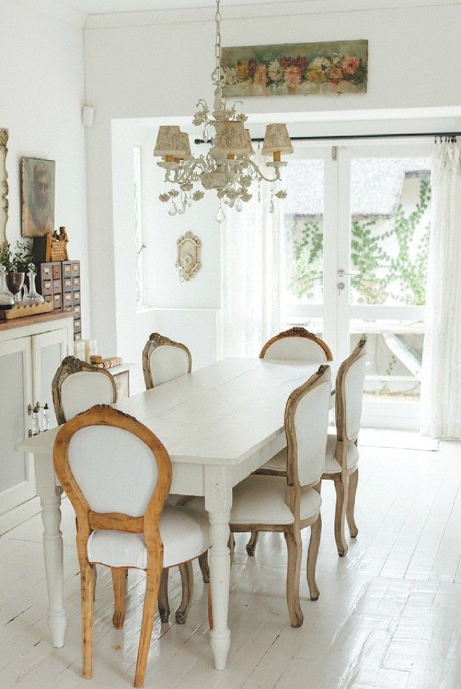 an adorable French chic dining room with a storage unit, vintage artworks, a white vintage table, vintage chairs and a chic chandelier