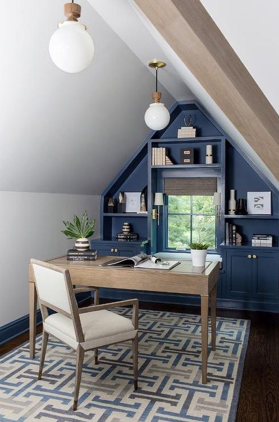 an elegant farmhouse attic home office with a blue accent wall with built-in storage, a stained desk and a neutral chair, pendant lamps