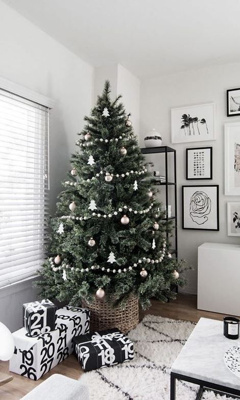 a Christmas tree with white and metallic ornaments and pompoms garlands and black and white gift boxes