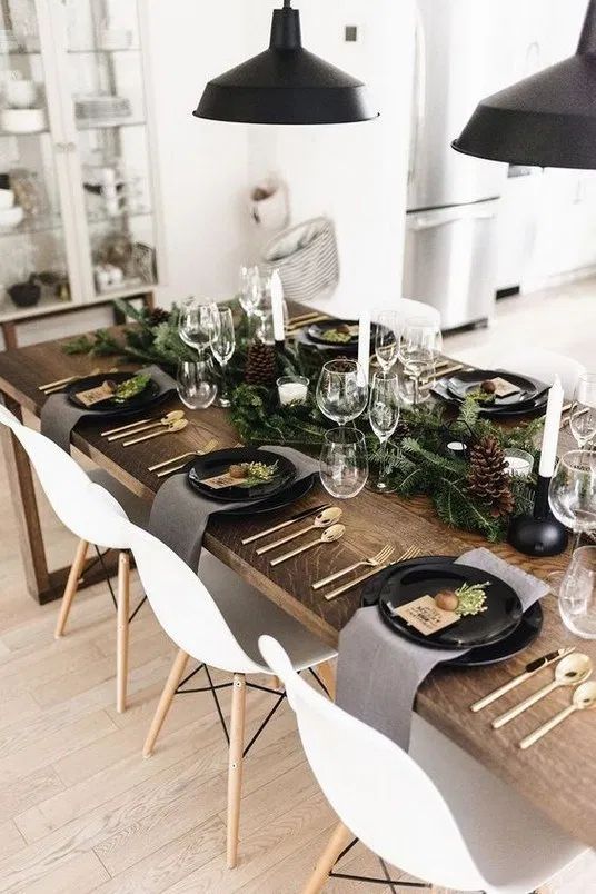 a Nordic rustic tablescape with an evergreen runner, pinecones, candles, black plates and grey napkins