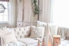 a beautiful vintage farmhouse Christmas space with a white sectional, fluffy pillows and blankets, a tray with white pillar candles and mini bottle brush trees