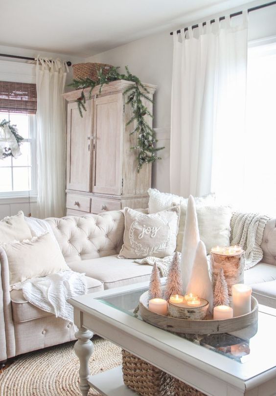 a beautiful vintage farmhouse Christmas space with a white sectional, fluffy pillows and blankets, a tray with white pillar candles and mini bottle brush trees