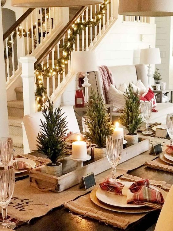 a chic rustic Christmas tablescape with a burlap runner, placemats, mini potted trees, candles and plaid napkins