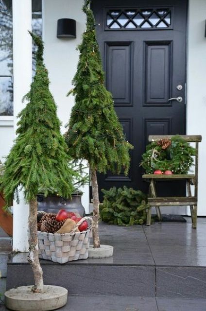 a cool Christmas porch with trees, a basket with pinecones and apples and a wreath with lights and pinecones