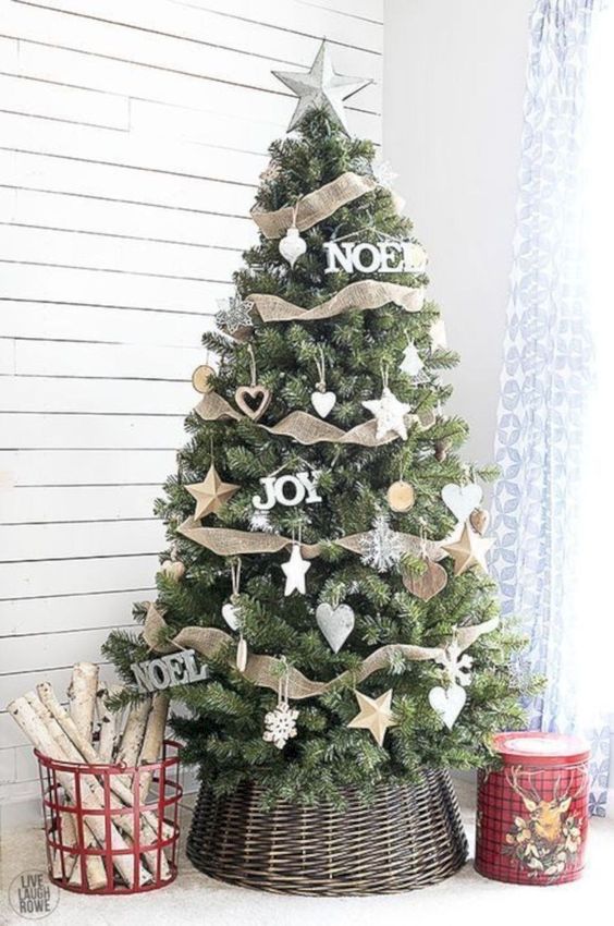 a farmhouse Christmas tree with burlap ribbons, white star and snowflake ornaments and firewood in a red basket