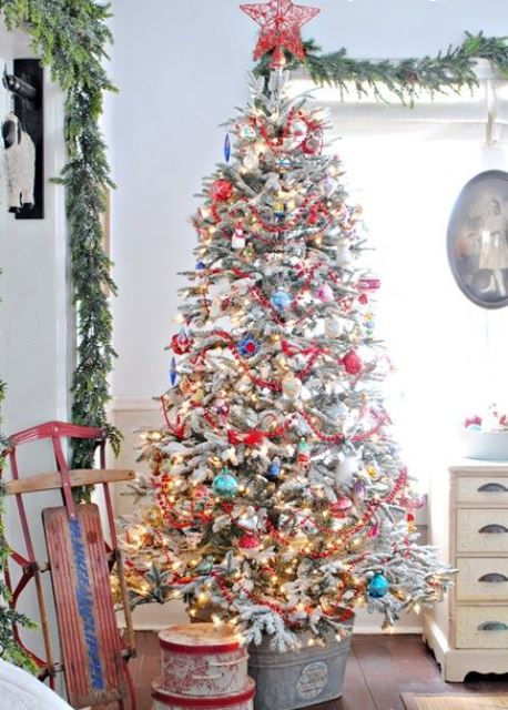 a flocked Christmas tree with colorful ornaments, lights and a red yarn star tree topper looks really vintage-like