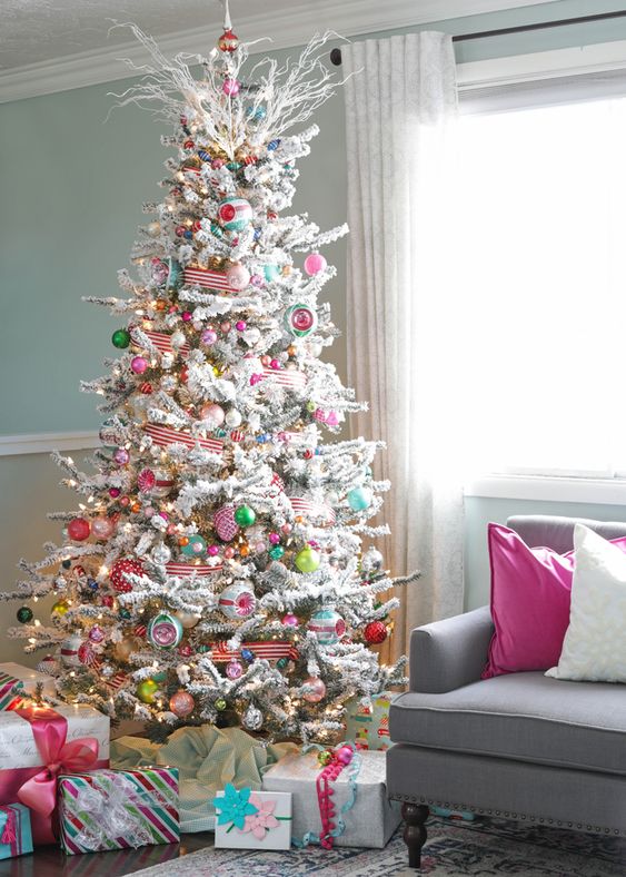 a flocked Christmas tree with lights, colorful ornaments, striped ribbons and frozen branches on the top