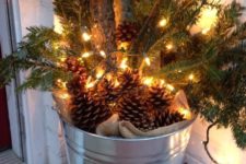 a galvanized bucket with burlap, pinecones, evergreens and branches is a cool rustic decoration for Christmas