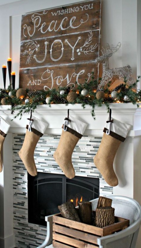 a large wooden plank Christmas sign, an evergreen garland with vine balls, pinecones and stockings of felt