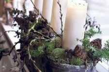 a metal bowl with moss, branches and pinecones and pillar candles as a Christmas decoration or centerpiece