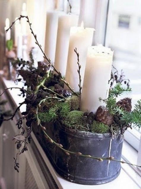 a metal bowl with moss, branches and pinecones and pillar candles as a Christmas decoration or centerpiece