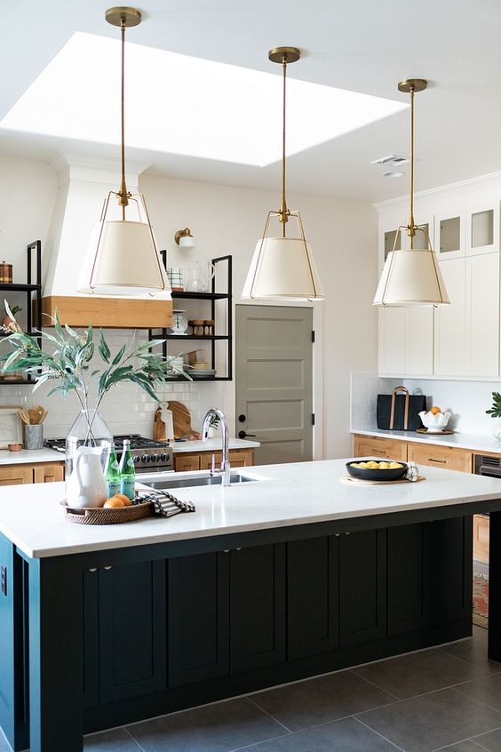 a modern farmhouse with stained cabinetry and a black kitchen island, white stone countertops, pendant lamps with brass touches and traditional lampshades