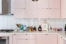 a modern pastel kitchen done in soft pink, with a catchy pendant lamp and a white square tile backsplash