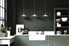 a moody kitchen with dark green brick walls, green cabinetry, white countertops and white pendant lamps is a statement