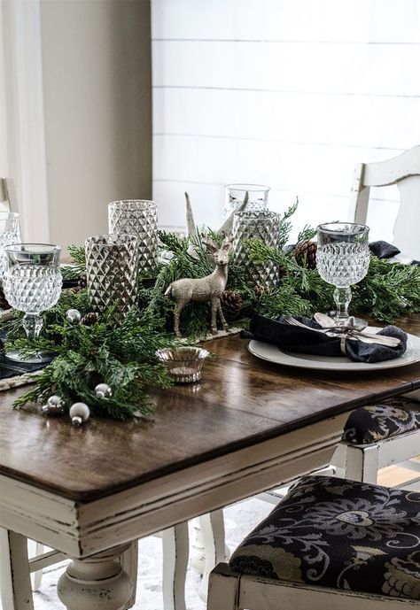 a moody rustic Christmas table with an evergreen runner, silver ornaments, vases and black napkins and a deer figurine