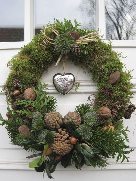 a natural Christmas wreath of moss, greenery, foliage, nuts, acorns, pinecones and a silver heart