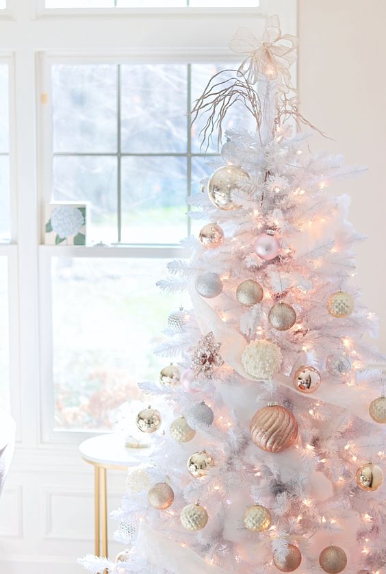 a pure white Christmas tree with gold, white and peachy pink ornaments and lights plus a bow tie and some twigs