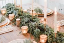 a refined rustic Christmas table with an evergreen runner, lots of candles, gilded chargers and evergreen touches