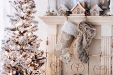 a refined vintage white Christmas space with a flocked Christmas tree with lights, a mantel with stockings and mini houses, a fur stool