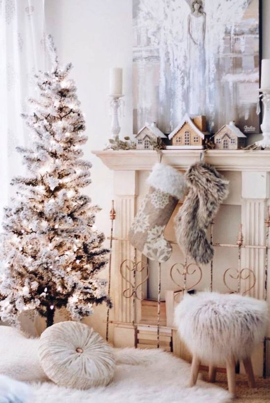 a refined vintage white Christmas space with a flocked Christmas tree with lights, a mantel with stockings and mini houses, a fur stool