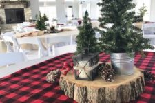 a rustic Christmas centerpiece of a wood slice, pinecones and mini trees in buckets plus a candle lantern