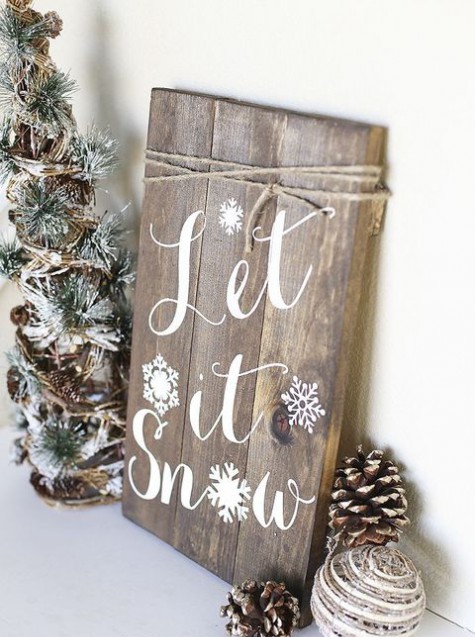 a rustic Christmas sign of wooden planks, pinecones and vine balls and mini Christmas trees with mini pinecones