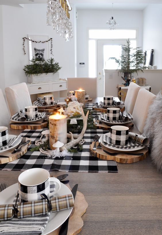 a rustic Christmas table with a buffalo check runner, mugs, napkins, antlers, a candle in a tree stump and some striped napkins