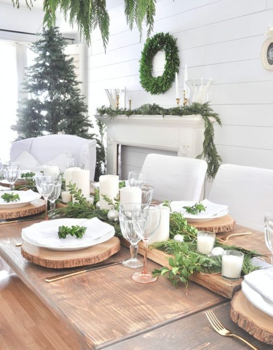 a rustic Christmas tablescape with an uncovered table, a greenery runner with candles, wood slice placemats