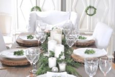 a rustic Christmas tablescape with wood slice chargers, an evergreen runner, candles and ornaments plus some greenery