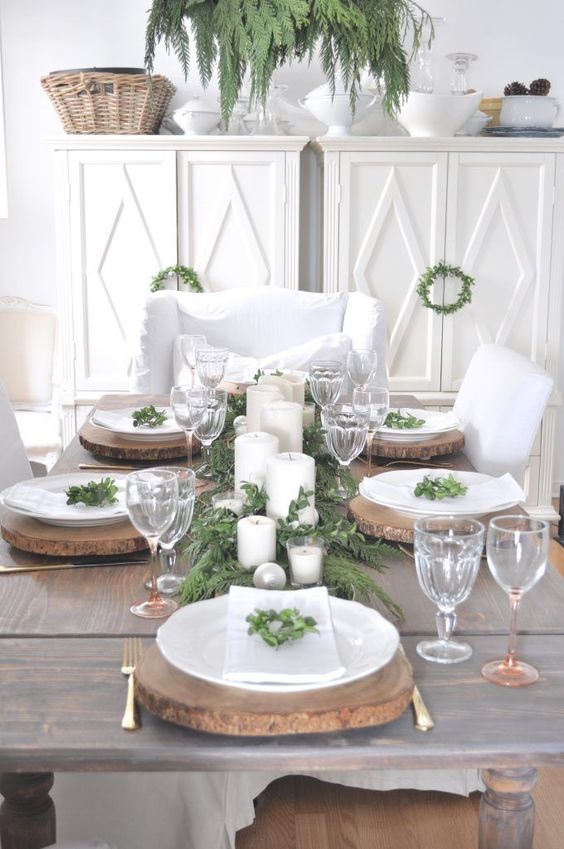 a rustic Christmas tablescape with wood slice chargers, an evergreen runner, candles and ornaments plus some greenery