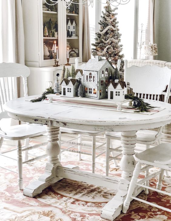 a shabby chic white table and chairs, a stand with houses and bottle brush trees for refined vintage Christmas decor
