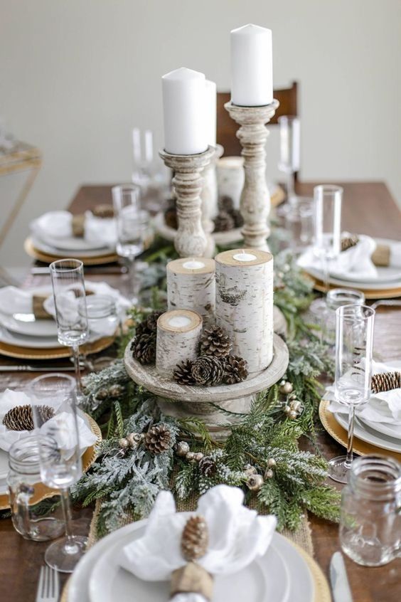 a snowt rustic Christmas table with a flocked evergreen runner, pinecones, branch candleholders, pinecone napkin rings