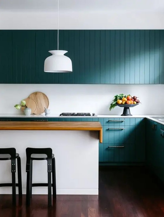 a stunning turquoise coastal kitchen with beadboard cabinets, a white kitchen island with a stained countertop, black stools and a white pendant lamp