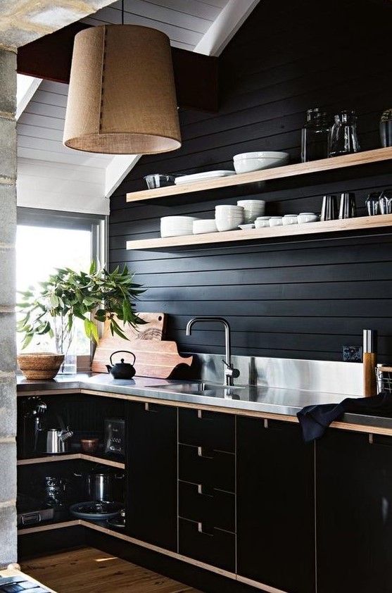 a stylish moody kitchen with black walls and cabinetry, metal countertops and a backsplash, a burlap pendant lamp