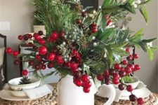 a white jug with lots of textural greenery, berries and fruits, woven placemats and printed porcelain for a rustic Christmas