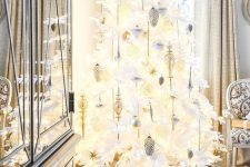a white lit up Christmas tree decorated with white, silver and gold ornaments, feathers and a large gold glitter star topper is wow