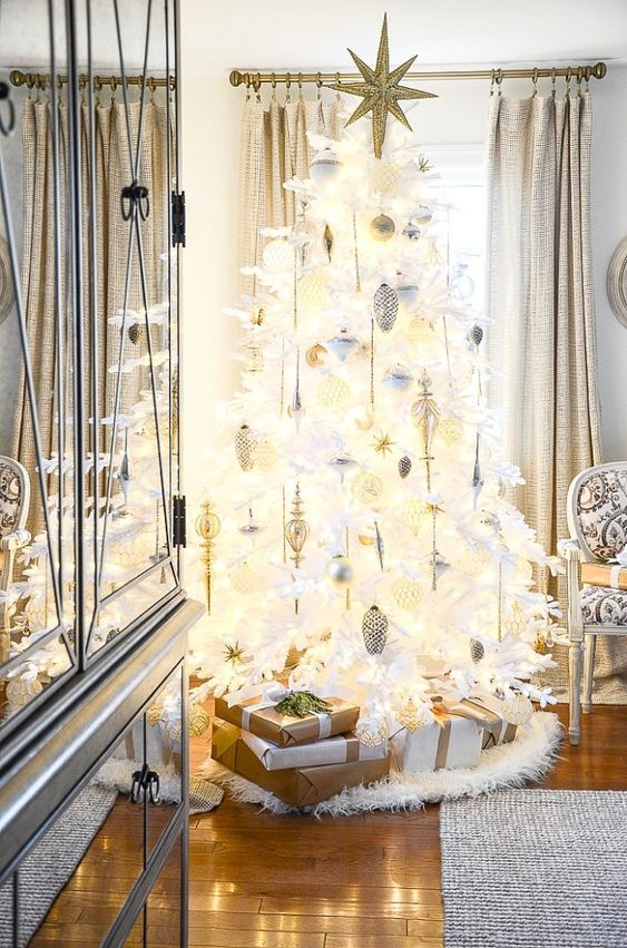 a white lit up Christmas tree decorated with white, silver and gold ornaments, feathers and a large gold glitter star topper is wow