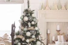 a white vintage Christmas space with a tree decorated with white, silver and green ornaments, a burlap and lace ribbon and white snowflakes, pillar candles and plywood trees
